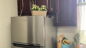 Un réfrigérateur Whirlpool en acier inoxydable dans une cuisine dotée de meubles en bois foncé et d’un plan de travail sur lequel se trouve un panier de fruits contenant des bananes et un ananas.