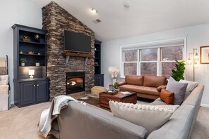 A living room with a stone fireplace, a leather sofa, and a television mounted on the wall. - SKI YA LATER Whitetail (Mercersburg)