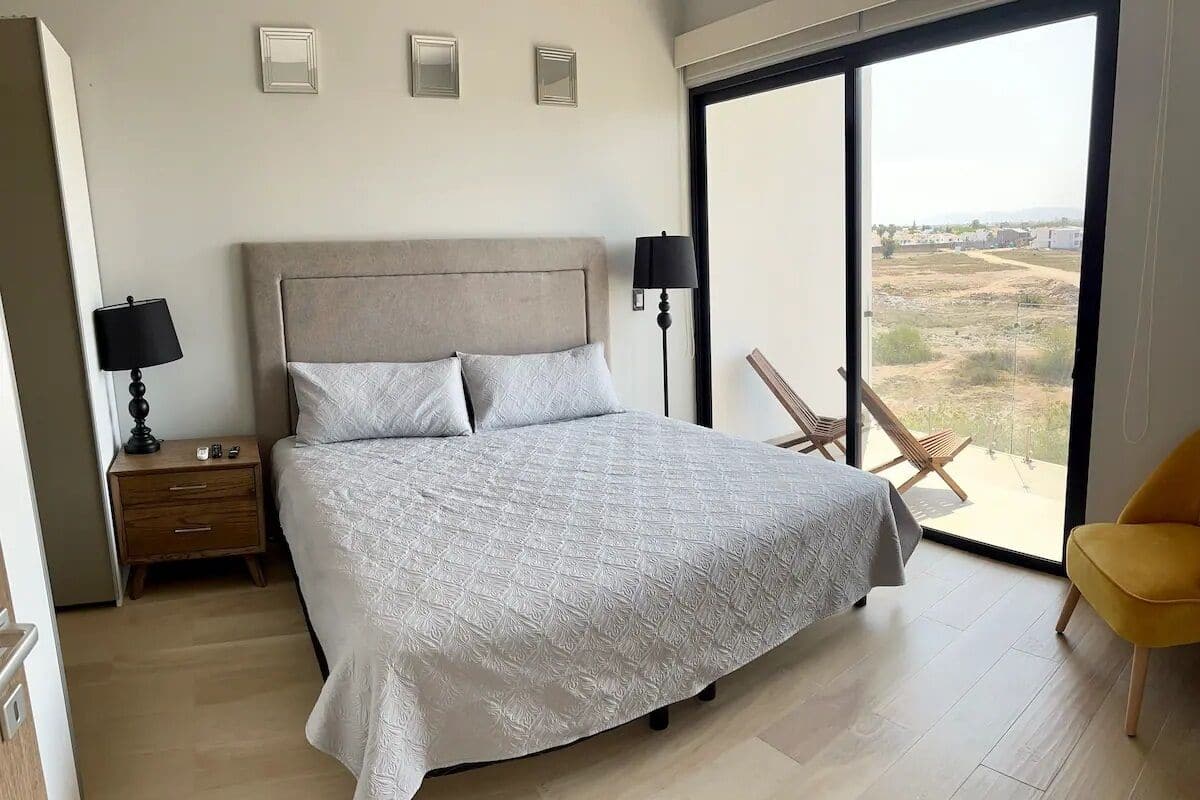 Une chambre avec un grand lit, deux tables de chevet avec des lampes, un fauteuil et un balcon avec vue.