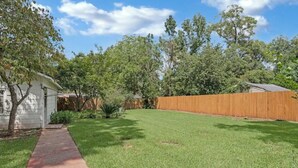 A backyard with a wooden fence, a grassy lawn, and a small shed. - Cheerful and chic- newly renovated home 4br/3b (Shreveport)