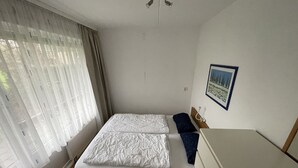 A bedroom with a bed, a dresser, a window with curtains, and a wall-mounted picture.