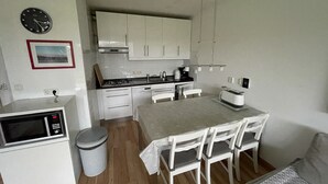 A compact kitchen with white cabinets, a microwave, a sink, and a dining table with chairs.