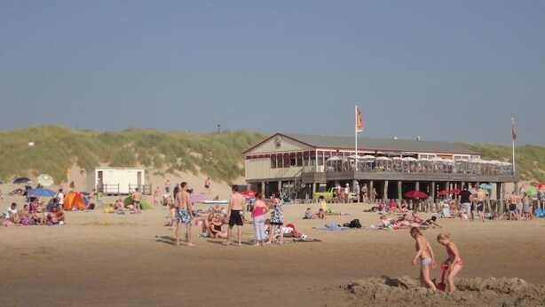 A beachside building with a flat roof, multiple windows, and a flag on top.