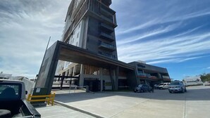 A multi-story building with a modern architectural design, featuring a prominent overpass structure. - Condos Ferrara (Mazatlán)