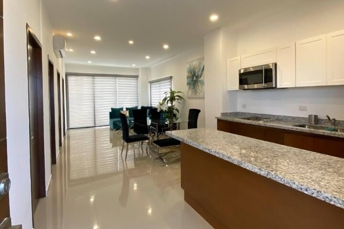 Una cocina moderna con gabinetes blancos, encimera de granito y electrodomésticos de acero inoxidable.