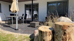 An outdoor patio area with a table and chairs, a covered umbrella, and a stone stump. - Beautiful apartment with large south-facing terrace (Sankt Peter-Ording)