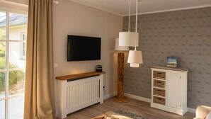 A modern living room with a large TV, a wooden cabinet, and a hanging light fixture. - Beautiful apartment with large south-facing terrace (Sankt Peter-Ording)