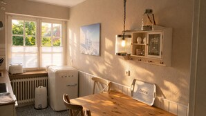 A kitchen with a wooden table and chairs, a vintage refrigerator, a window with blinds, and a hanging light fixture. - Beautiful apartment with large south-facing terrace (Sankt Peter-Ording)
