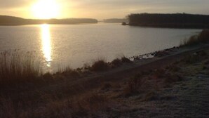 A calm lake at sunrise with a visible shoreline and distant trees. - 6 pers. Apartment, 3 sep. Sleeping room, 300 m v. Beach, constantly modernized and clean  (Westkapelle, Zeeland / Walcheren)
