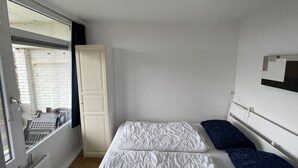A small room with a bed, a window, a white wardrobe, and a radiator. - 6 pers. Apartment, 3 sep. Sleeping room, 300 m v. Beach, constantly modernized and clean  (Westkapelle, Zeeland / Walcheren)
