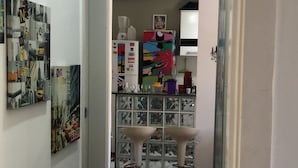 A narrow hallway with a tiled floor leading to a room with a ceiling fan, a refrigerator, and a colorful cabinet with various items.