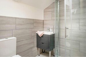 A modern bathroom with grey tiles, a glass shower enclosure, a white sink, and a dark-colored cabinet. - 2-bed Cottage Sleeps 4 With Hot Tub (Honiton)
