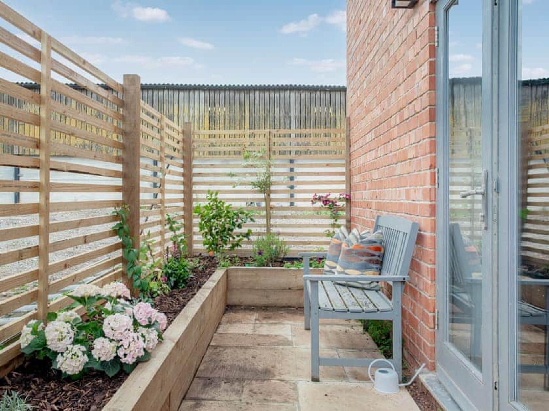 Un patio con valla de madera, un banco y una jardinera con flores.