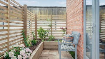 Un patio con valla de madera, un banco y una jardinera con flores.