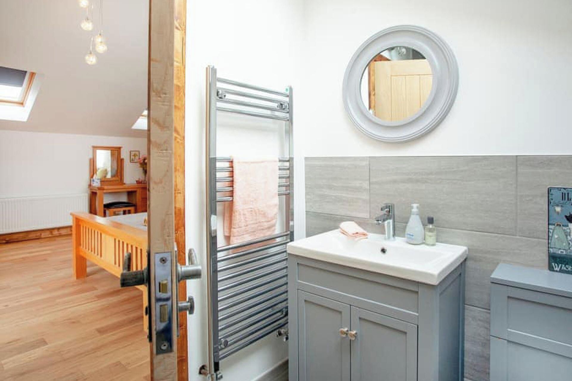 A modern bathroom with a glass shower enclosure, a round mirror, and a sink with toiletries.