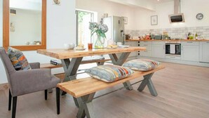 Une cuisine moderne avec une table à manger en bois, deux bancs et une chaise recouverte d’un tissu gris.
