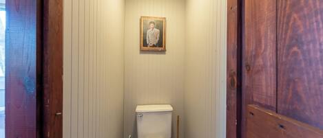 Une petite salle de bain aux murs en bois, avec des toilettes blanches, une brosse de toilette verte et un tableau encadré accroché au mur.