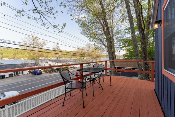 A wooden deck with a table and chairs, overlooking a street with a blue car parked on the side.