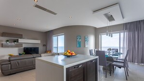 Una sala de estar moderna con un sofá, un comedor con mesa de vidrio y una isla de cocina con fruta.