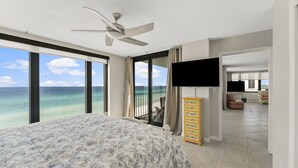 Quarto com uma cama grande, um ventilador de teto, uma TV e vista para o mar.