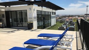 Una terraza en la azotea con sillones azules, un edificio moderno con ventanas amplias y vistas a la ciudad.