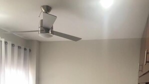 Un dormitorio con una cama, ventilador de techo, lámpara de noche y armario.