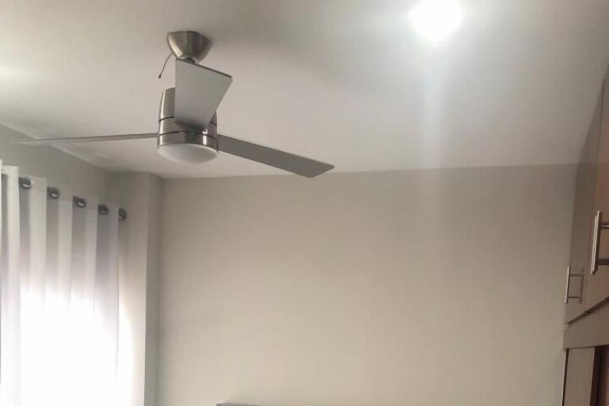 A bedroom with a bed, a ceiling fan, a bedside lamp, and a wardrobe.
