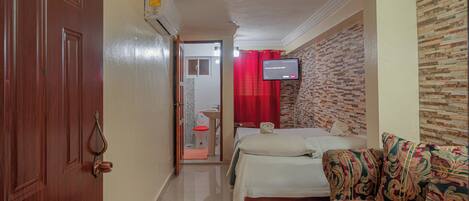 A hotel room with a bed, a sofa, a television mounted on the wall, and a bathroom visible through an open door.