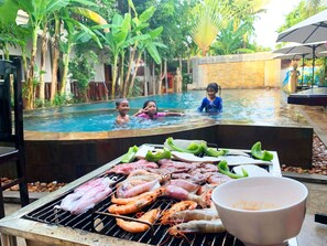 A poolside barbecue with grilled meats and seafood, surrounded by lush greenery and a swimming pool. - Lucky Courtyard Boutique Pool Villa (Siem Reap)