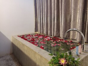 A bathtub filled with water and rose petals, a metal faucet, and a plant with yellow flowers. - Lucky Courtyard Boutique Pool Villa (Siem Reap)