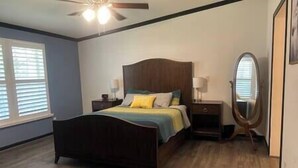A bedroom with a wooden bed, a nightstand, a mirror, and a ceiling fan. - The K Way, The K Way (Ocala)