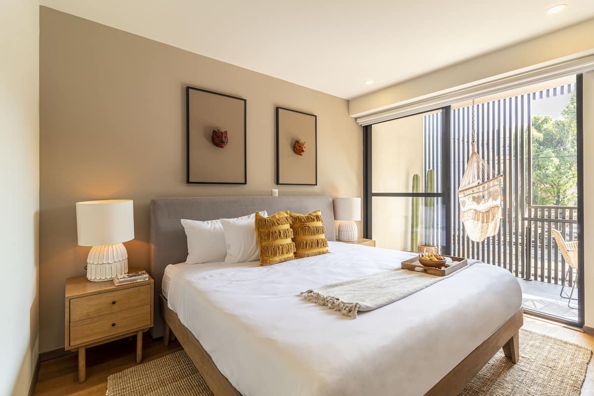 A bedroom with a large bed, two framed animal heads on the wall, a nightstand with a lamp, and a balcony with a hanging chair.
