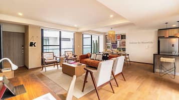 Un amplio salón con sofá, sillones, una mesa de centro y un comedor, con una cocina al fondo.