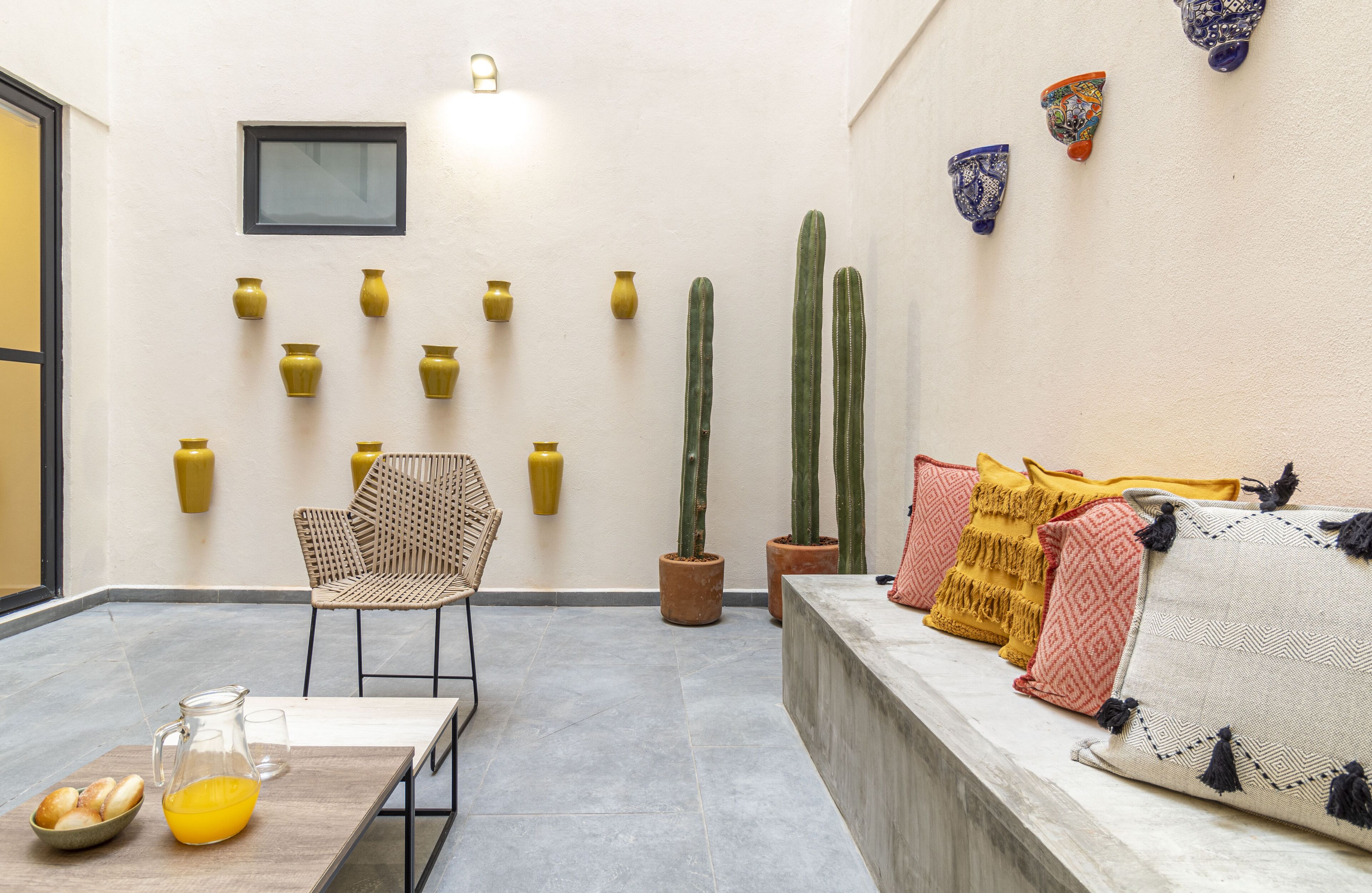 A cozy interior with a seating area, a table with a pitcher and bread, and a row of cacti against the wall.