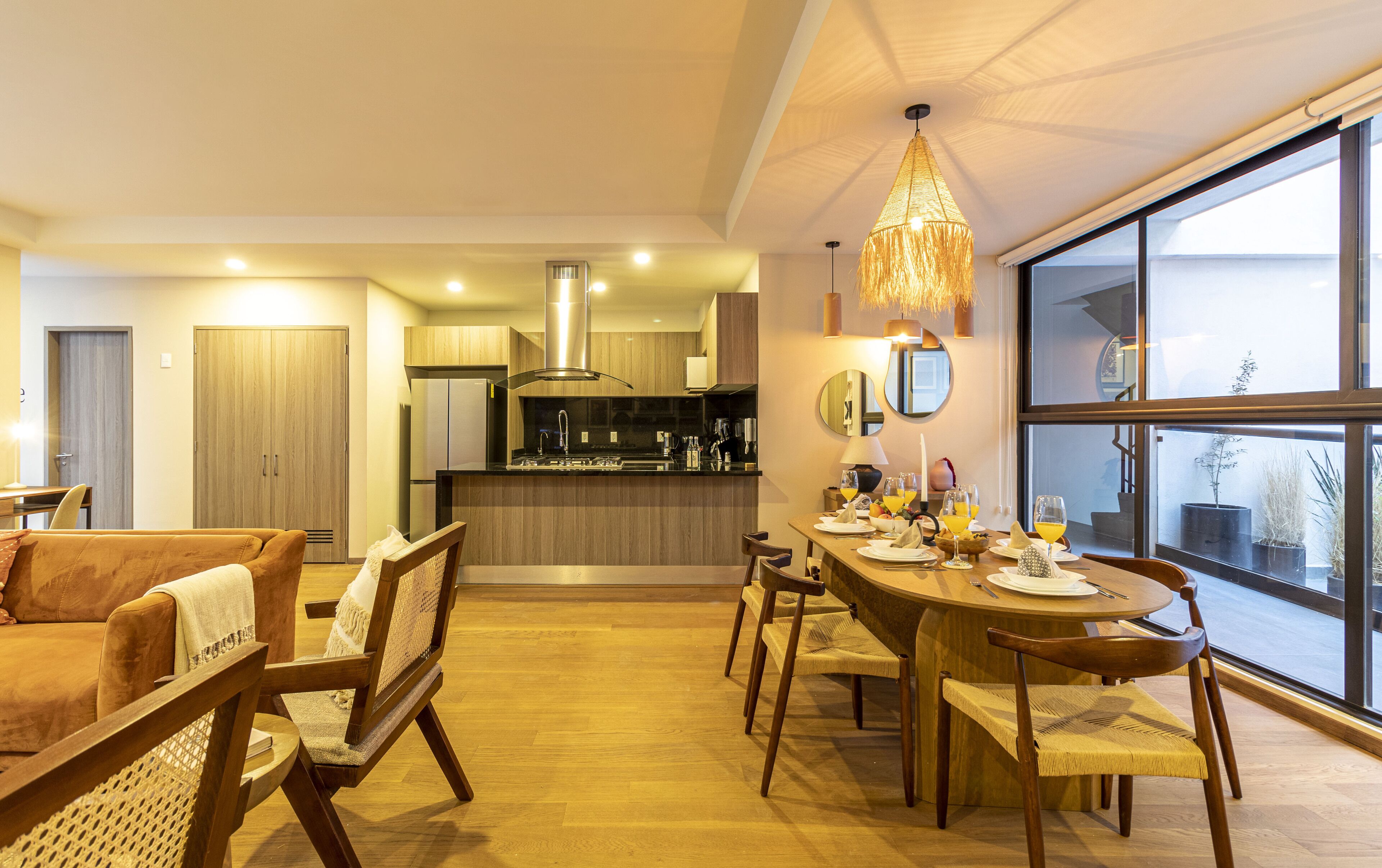 A modern kitchen with a central island, wooden dining table with chairs, and a large window providing a view of the outdoors.