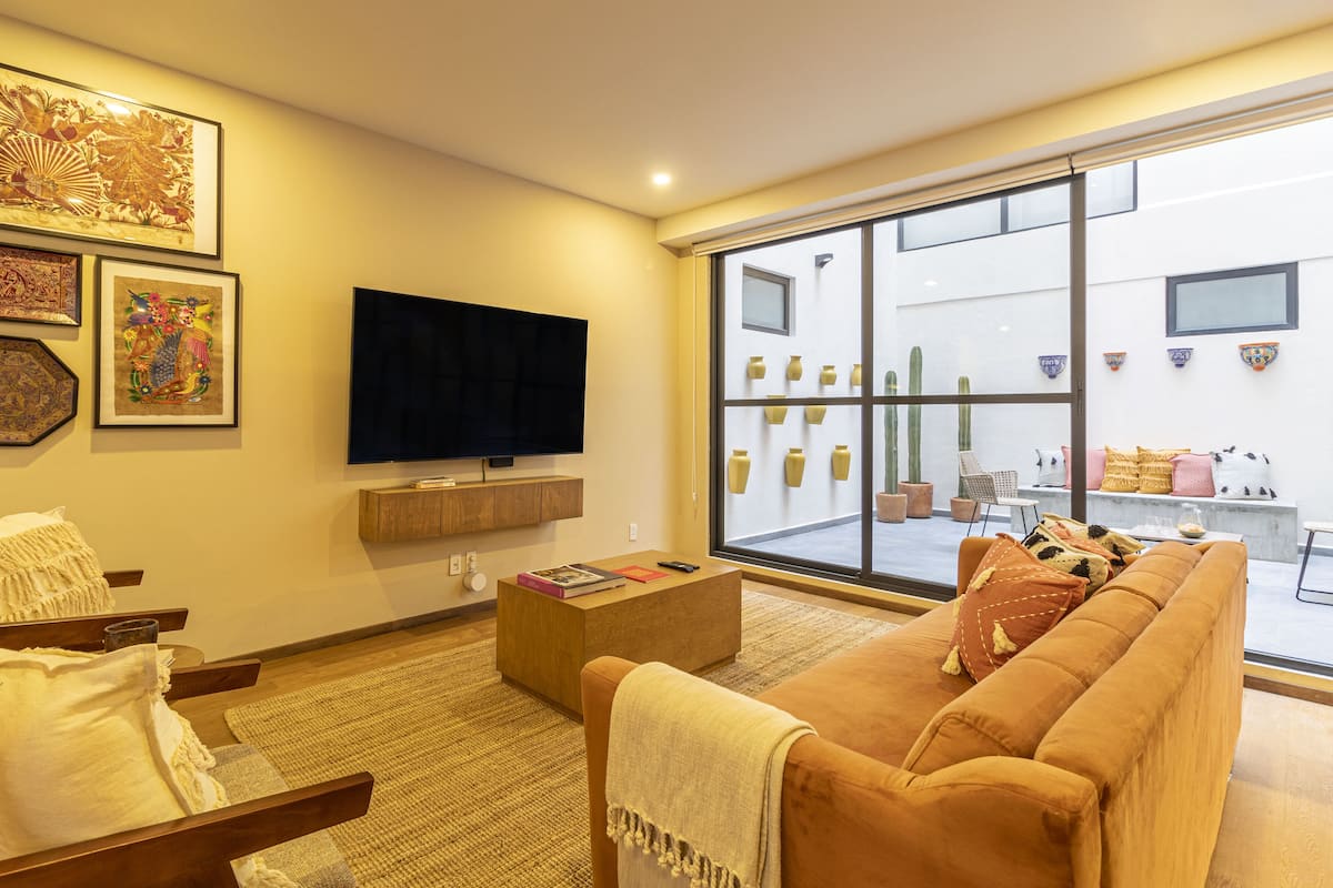 A living room with a large TV, comfortable seating, and a view of the outside.