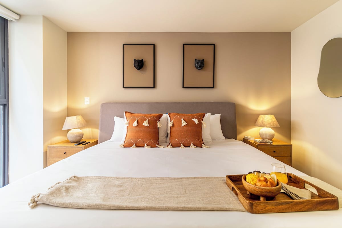 A neatly made bed with two pillows, a bedside table with a lamp, and a tray with fruits and a glass of juice.