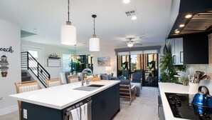 Cocina moderna con una isla central, luces colgantes y vistas a un comedor.