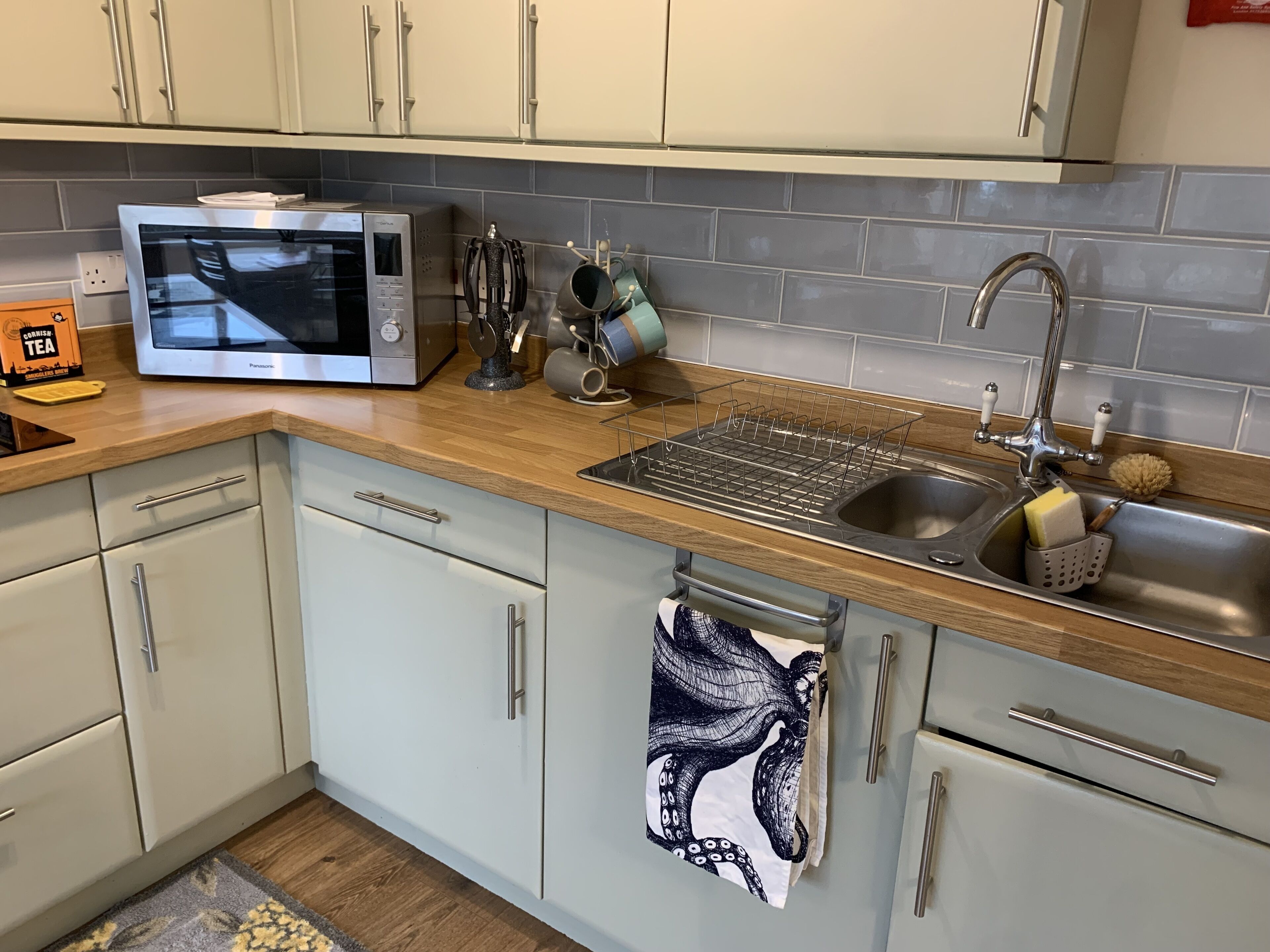 A kitchen with white cabinets, a microwave, a sink with a dish rack, and a towel hanging on the door.