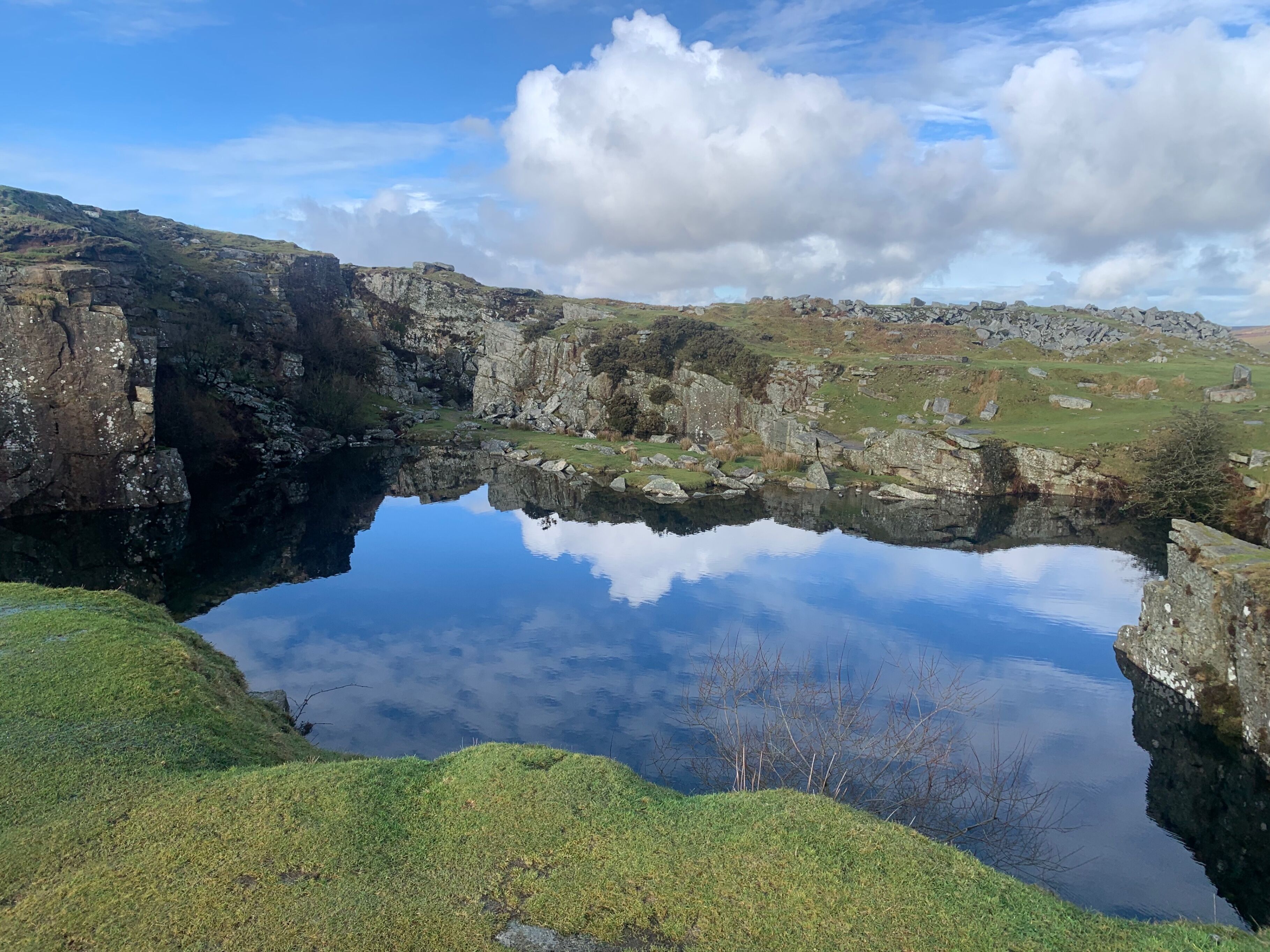 A natural landscape with a clear water body surrounded by rocky terrain and grassy areas.