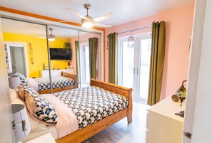 A bedroom with a wooden bed, a ceiling fan, a large mirror, and a sliding glass door leading to a balcony.
