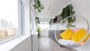 Una cocina moderna con armarios blancos, un sillón colgante con un cojín de colores, y vistas al exterior.