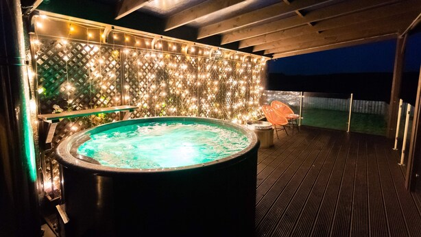 Un jacuzzi con terraza de madera y un muro decorativo con luces.