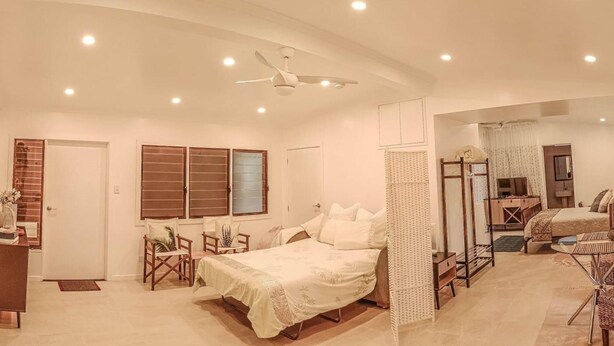 Ein geräumiges Schlafzimmer mit einem großen Bett, einem Deckenventilator und Blick in einen anderen Raum.