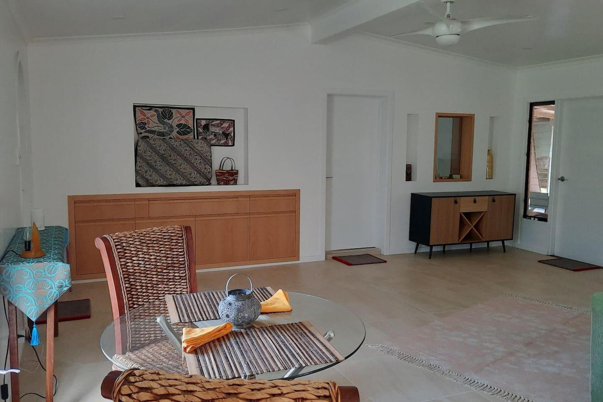 A spacious living room with a glass dining table, a patterned sofa, a wooden cabinet, and a ceiling fan.