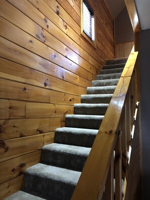 A wooden staircase with a handrail, carpeted steps, and a window with blinds.