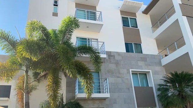Um edifício residencial de vários andares com varandas, grandes janelas e palmeiras em primeiro plano.