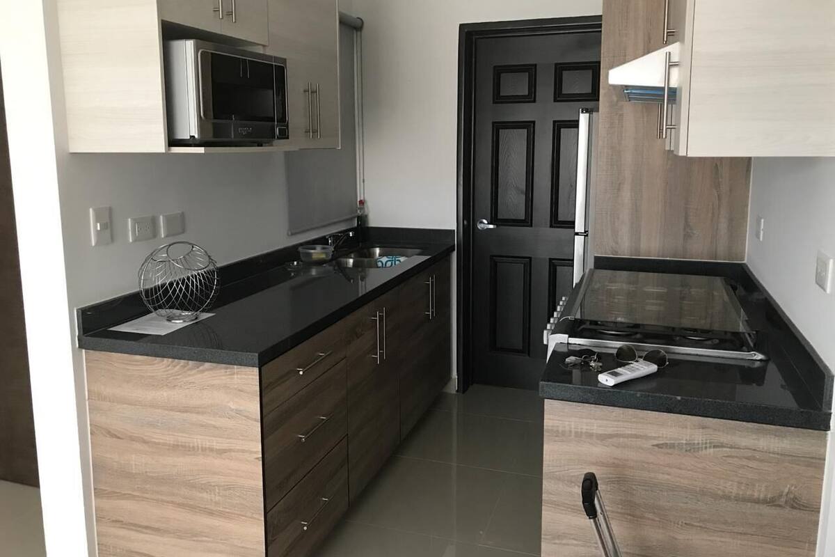 A modern kitchen with wooden cabinets, a black countertop, a microwave, and a stove.