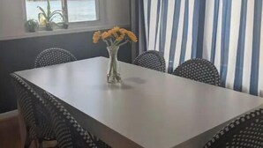 A dining area with a white table, black and white patterned chairs, a vase with yellow flowers, and a view of the water through a window.