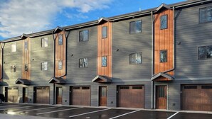 En række moderne, fleretagers bygninger med store garagedøre og en parkeringsplads foran.